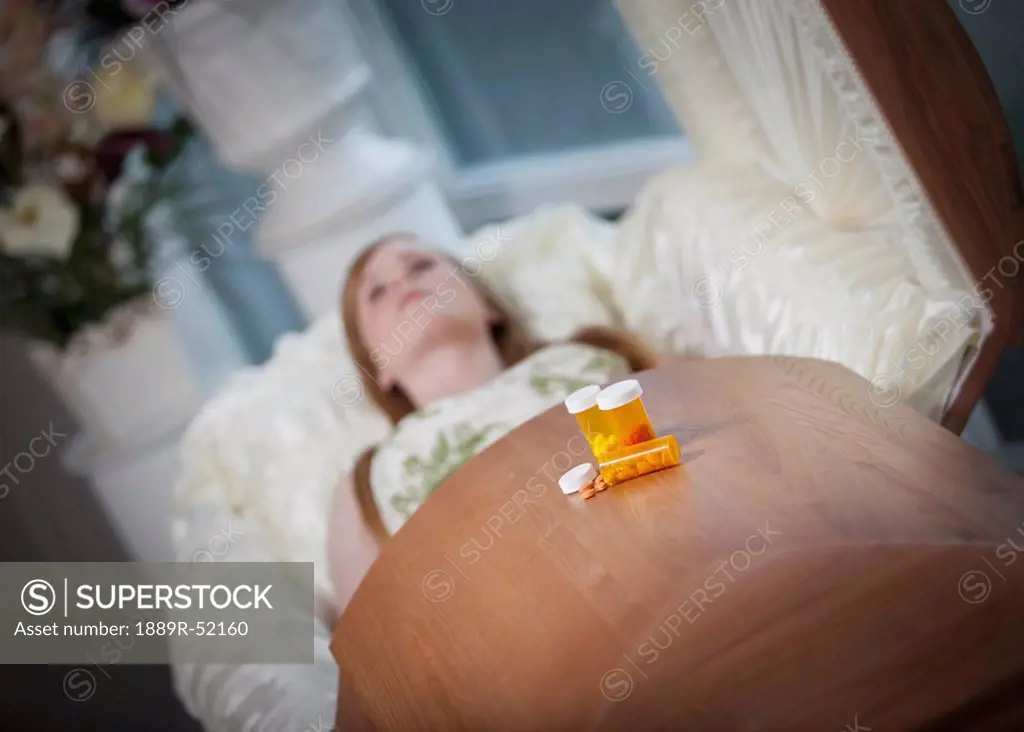 the coffin of a young woman with medication bottles on top