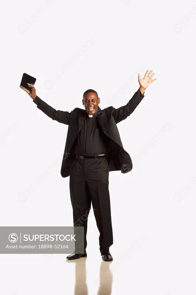 a man wearing a clerical collar and holding a bible with hands raised