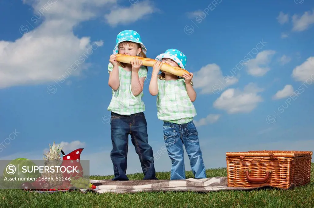 two young girls eating a big loaf of bread at a picnic