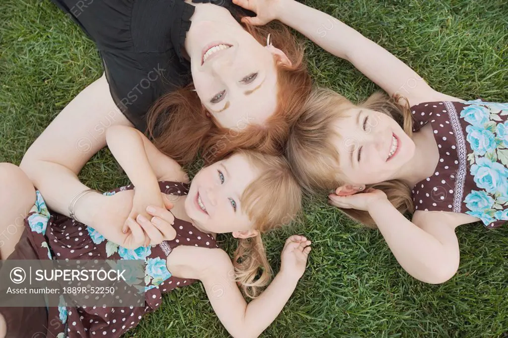 a mother laying on the grass with her two daughters