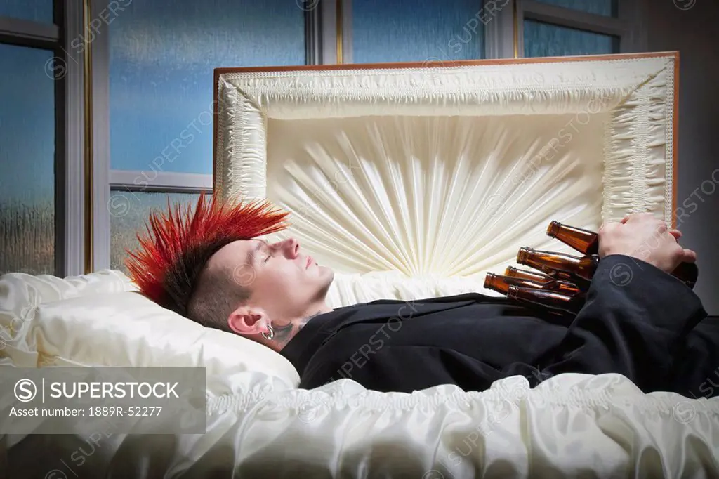 a deceased young man in a coffin holding beer bottles