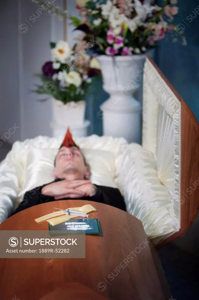 a deceased young man in a coffin with syringes laying on top
