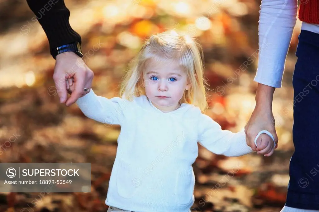 a young girl holding the hands of her parents