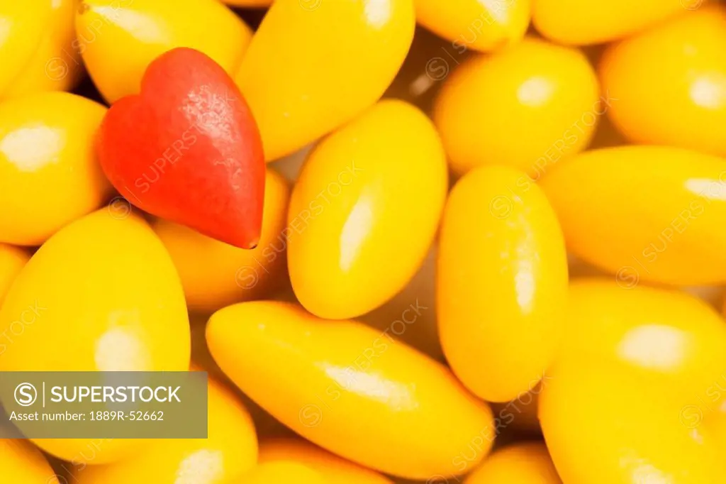 a red heart shaped candy on a pile of yellow candies
