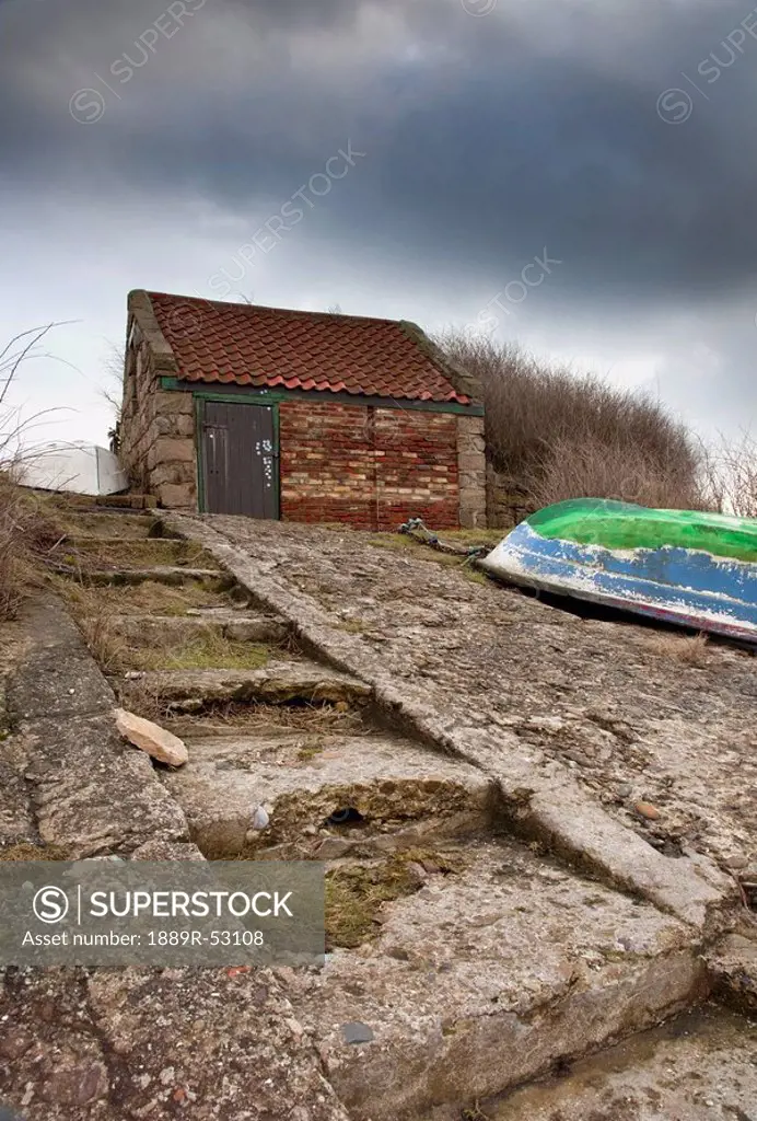 northumberland, england, a boat upside down on the shore with a wooden shed and dark clouds
