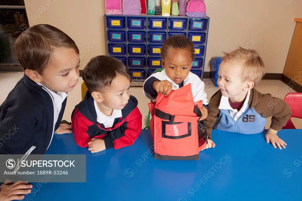 fort lauderdale, florida, united states of america, four young boys sitting at a table in a classroom looking into a lunch bag