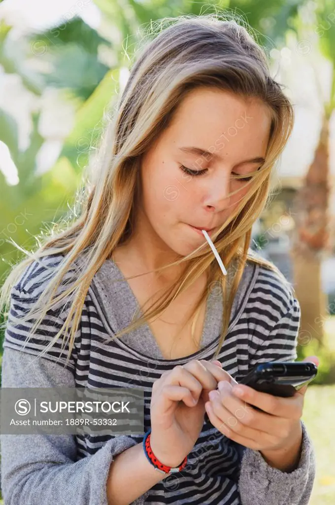 a preteen girl eating a sucker and using her cellphone