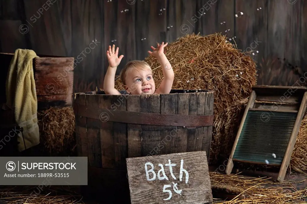 a toddler having a bath in a wooden barrel