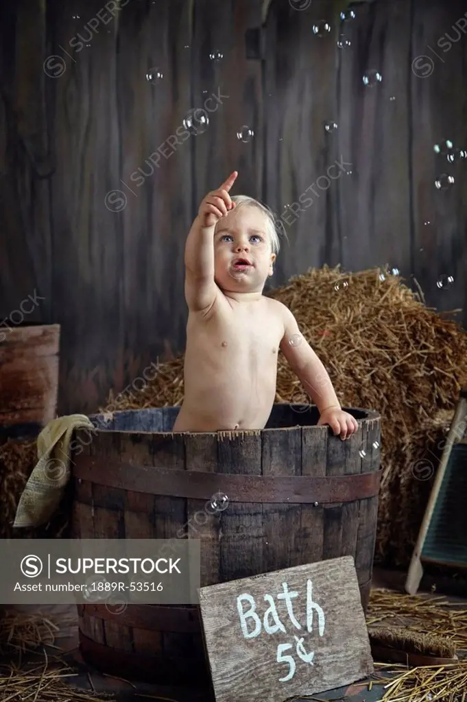 a toddler having a bath in a barrel and popping bubbles