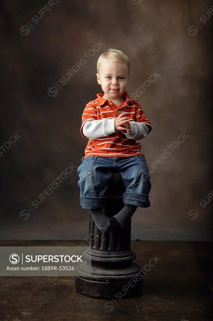 a toddler sitting on a pillar as a stool