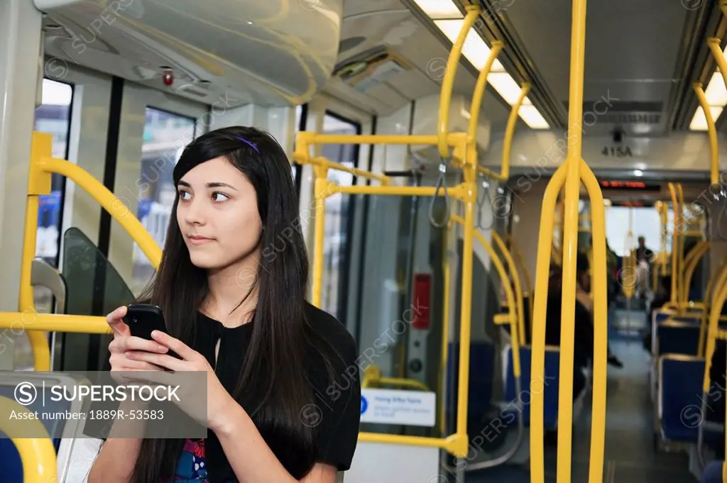 portland, oregon, united states of america, a teenage girl using her cell phone while sitting on public transportation