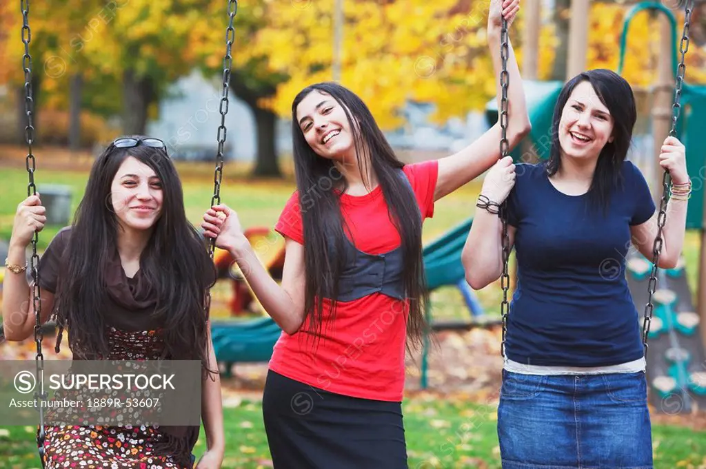 three teenage girls on swings at a playground