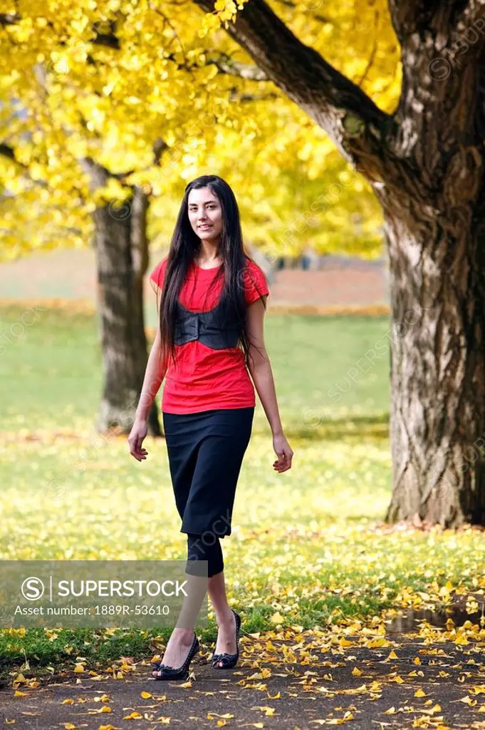 a teenage girl walking through a park in autumn