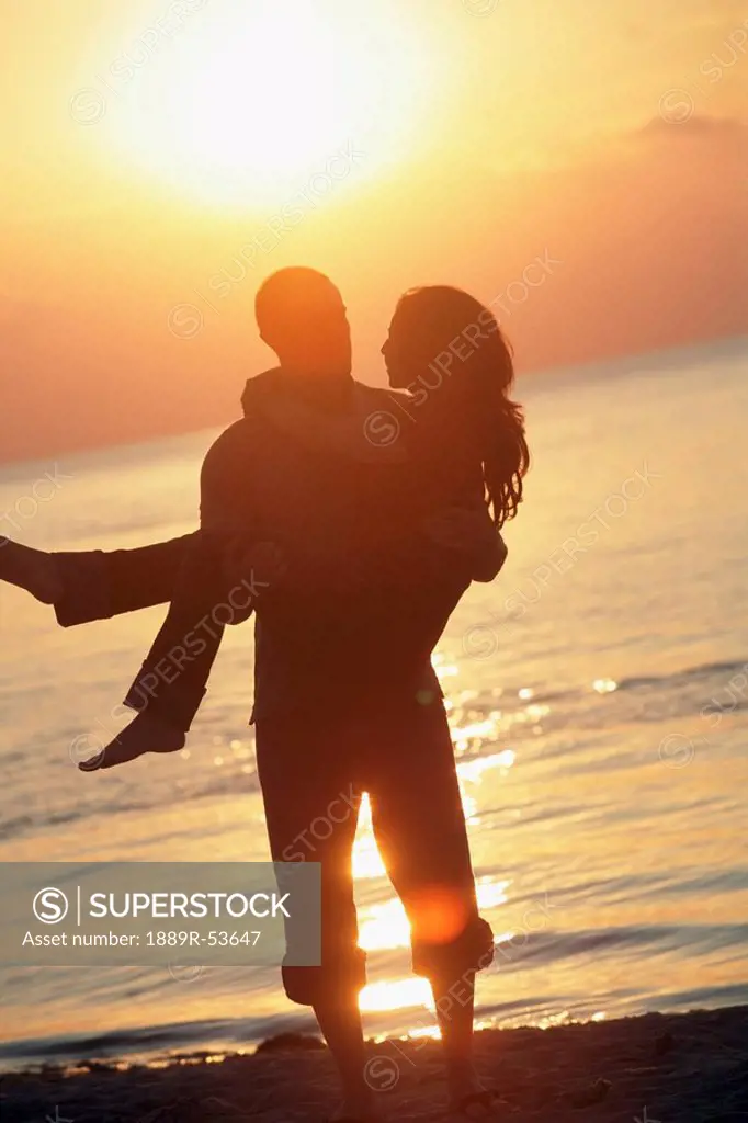 a man holding a woman on a beach in the sunset