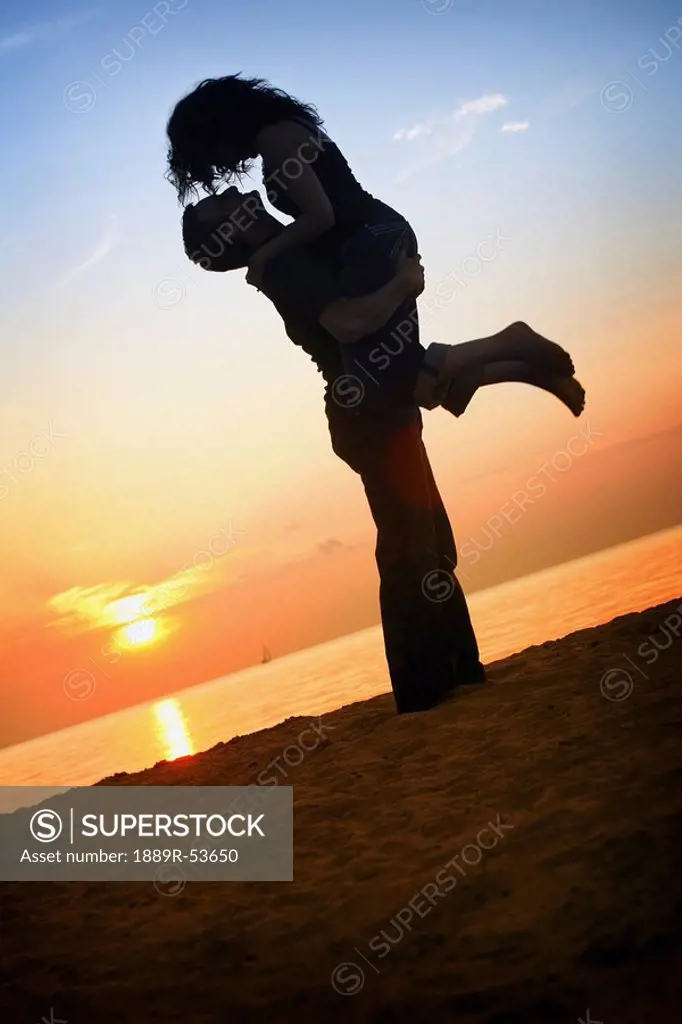a man and woman together on a beach in a sunset