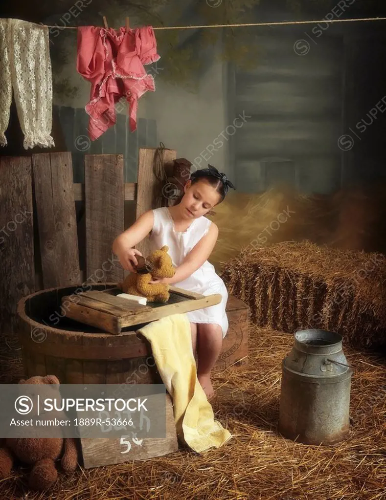 a girl washing her teddy bear in a barn