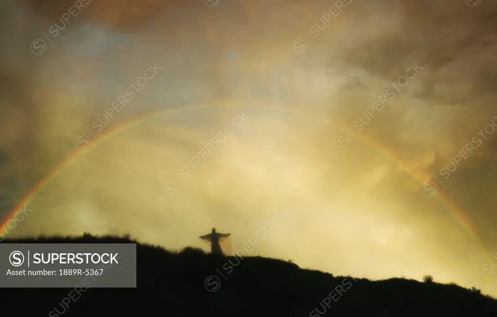 Rainbow over angel on hill
