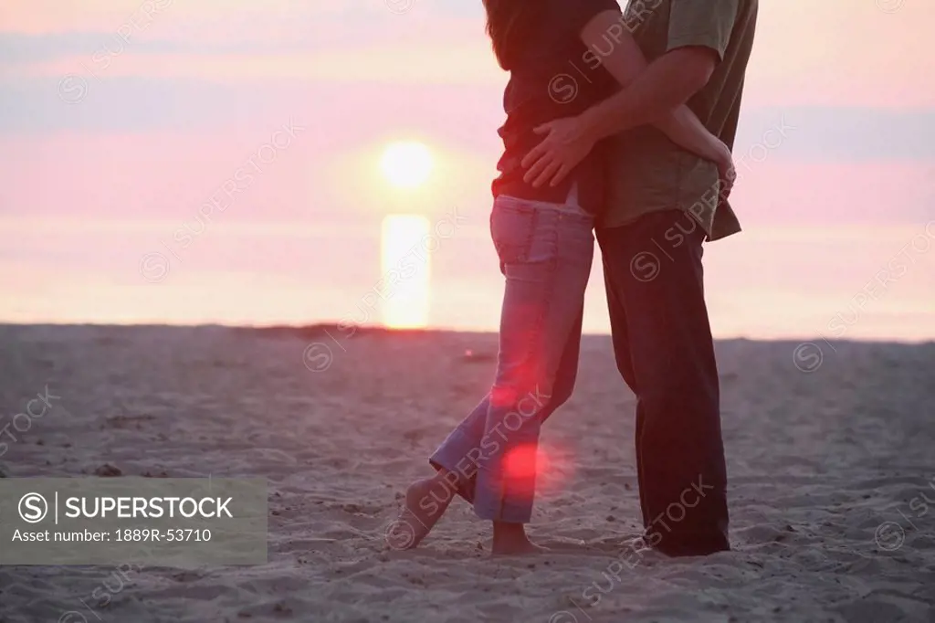 a couple standing together on a beach at sunset