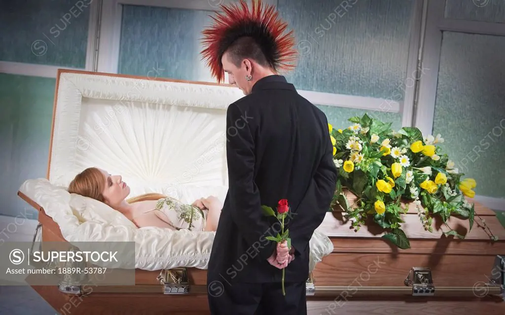 a man holding a rose and viewing a deceased woman laying in a coffin
