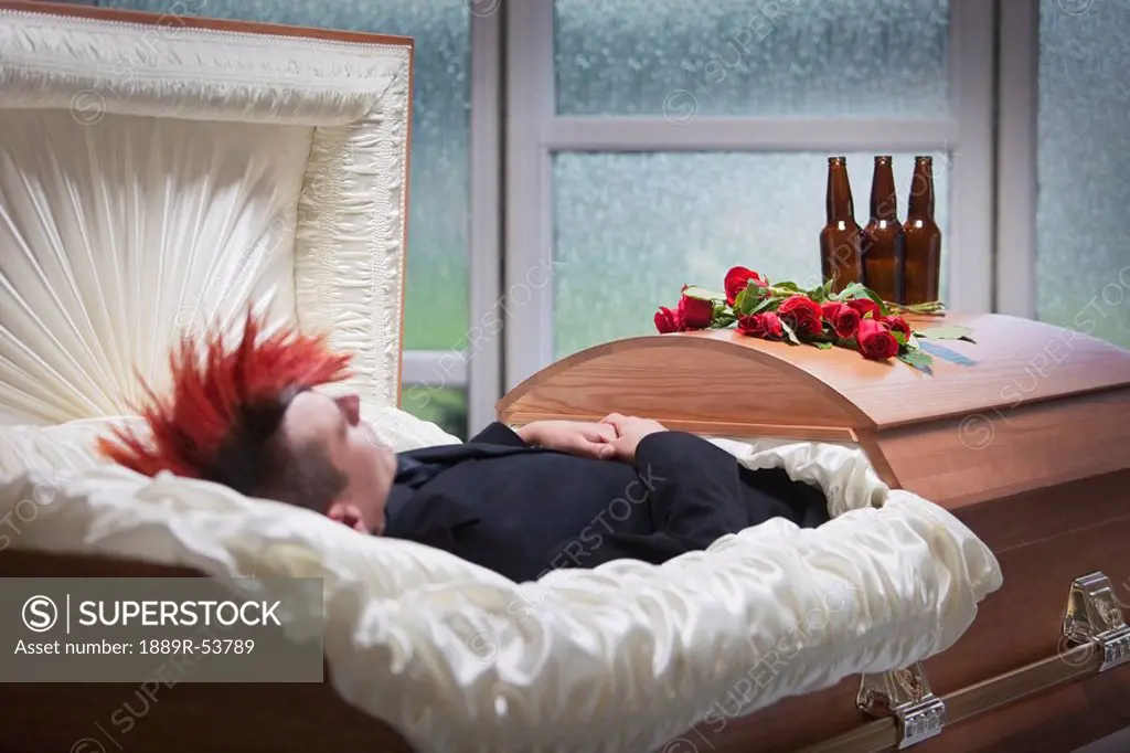 a deceased young man laying in a coffin with beer bottles on top of it