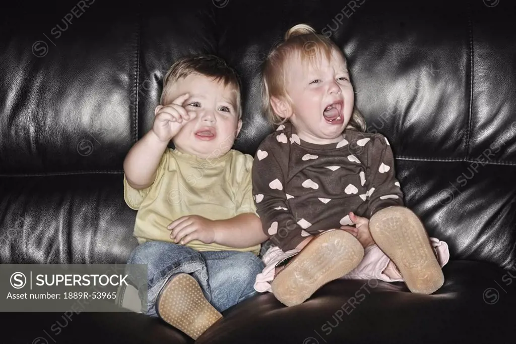 edmonton, alberta, canada, two young children sitting on the couch together and crying