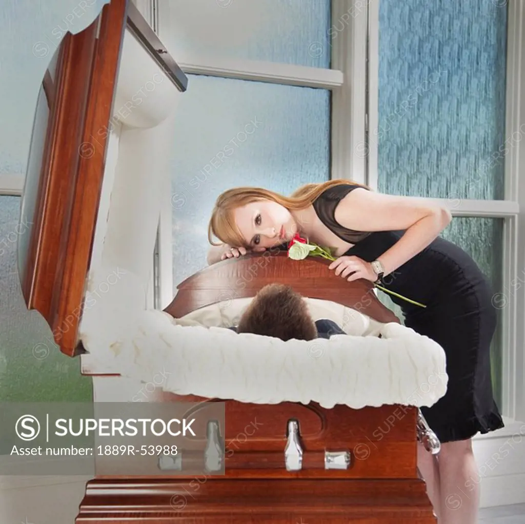 edmonton, alberta, canada, a young woman holds a rose and lays her head on the coffin of a deceased loved one