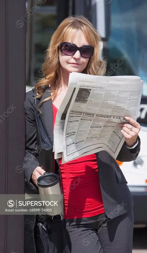 st. albert, alberta, canada, a woman reads the newspaper and holds her travel mug as she waits for the bus