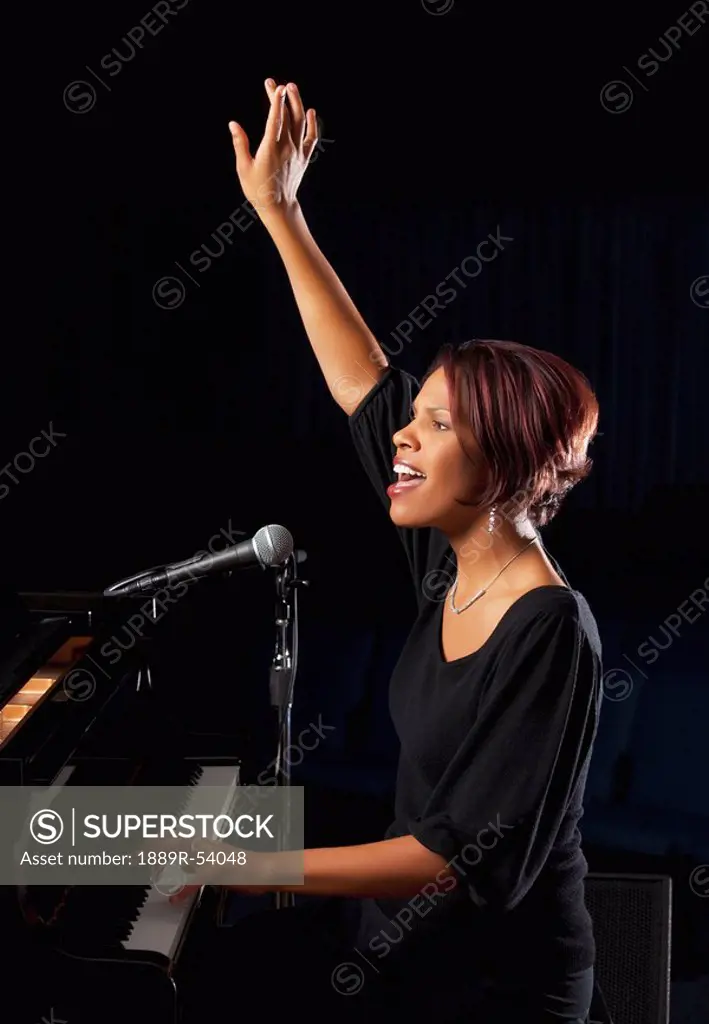 fort lauderdale, florida, united states of america, a woman playing the piano and singing in worship with her hand raised