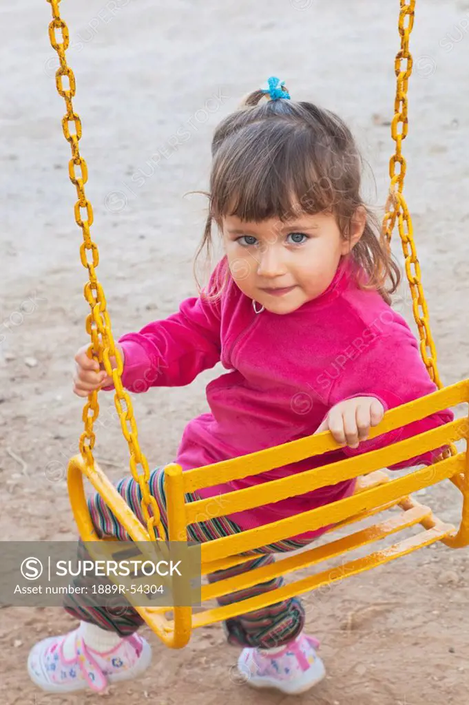 A Young Girl Sitting On A Yellow Swing