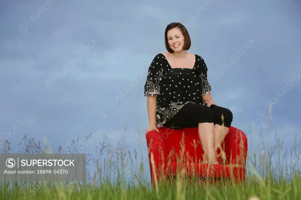 a woman sitting on a red chair in a field