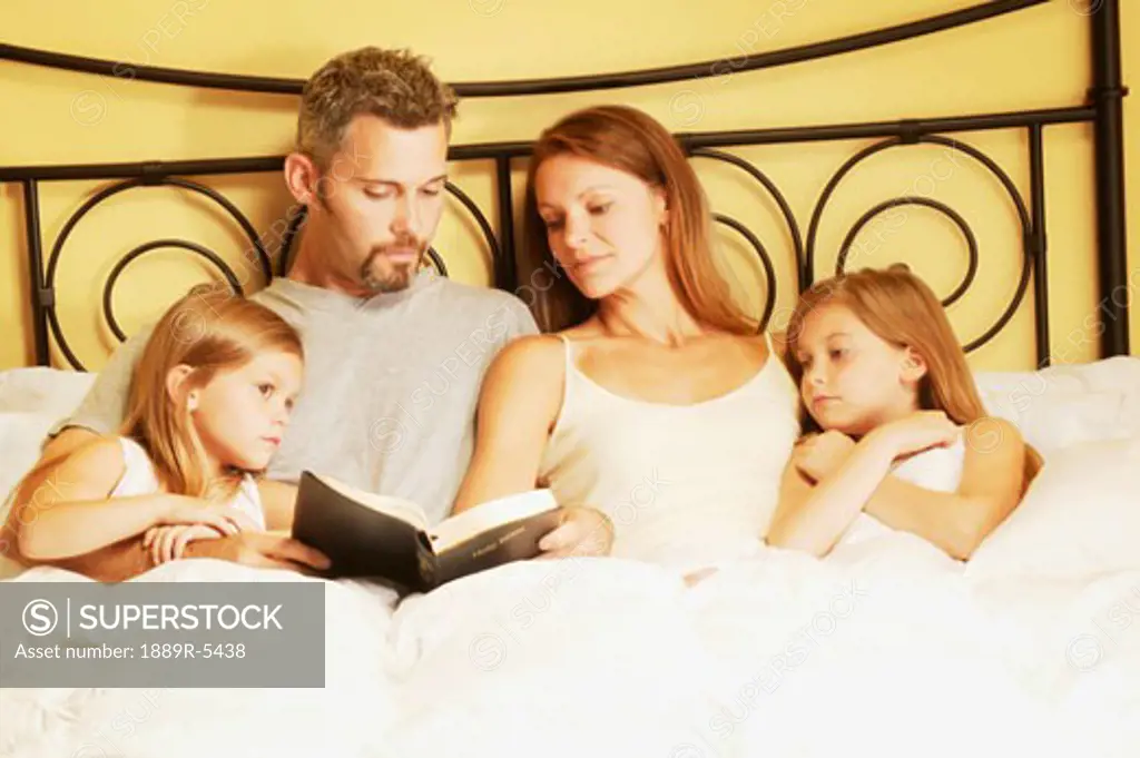 Family in bed reading bible