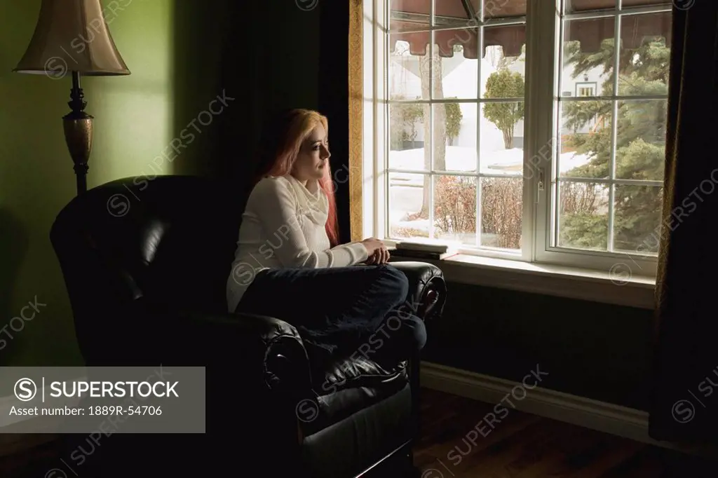 A Woman Sitting In A Large Chair Looking Out The Window