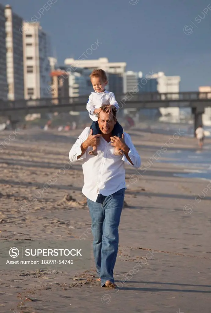 Fort Lauderdale, Florida, United States Of America, A Father Walking On The Beach With His Son On His Shoulders