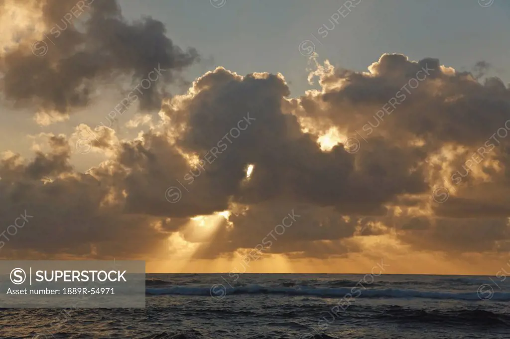 Sun Rays Spread From Clouds At Sunrise Over The Ocean