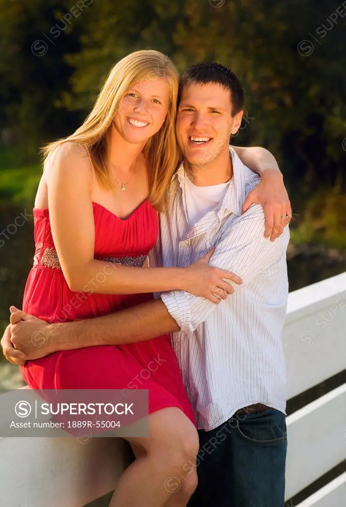 Willmar, Minnesota, United States Of America, A Woman Sitting On A Fence In An Embrace With A Man
