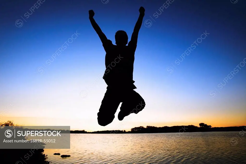 Willmar, Minnesota, United States Of America, Silhouette Of A Person Jumping In The Air By The Water At Sunset