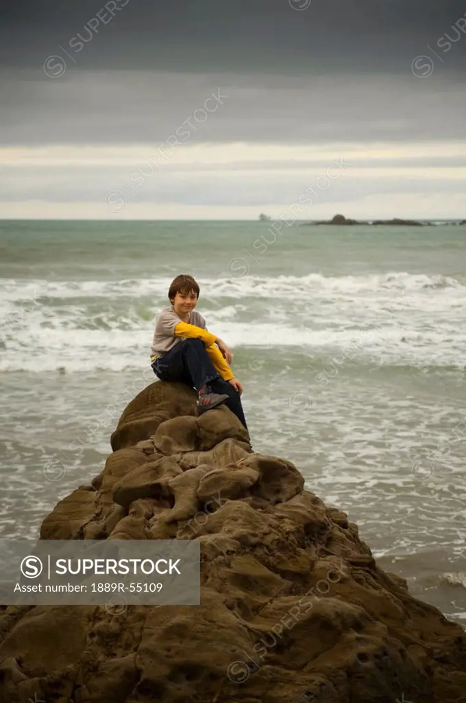 a boy sits on a rock at the water´s edge