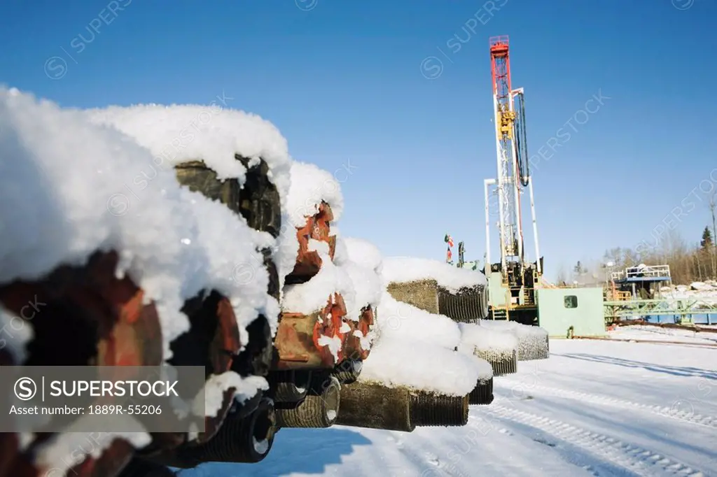 edson, alberta, canada, snow covered drilling pipes with a rig in the background