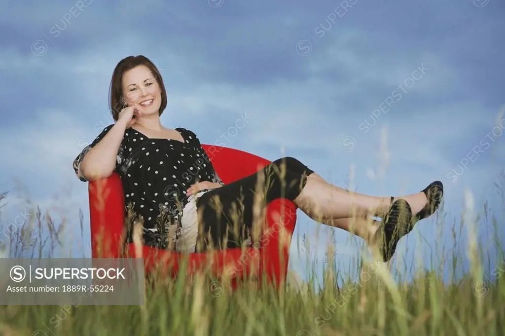 a woman sitting in a red chair in the middle of a field