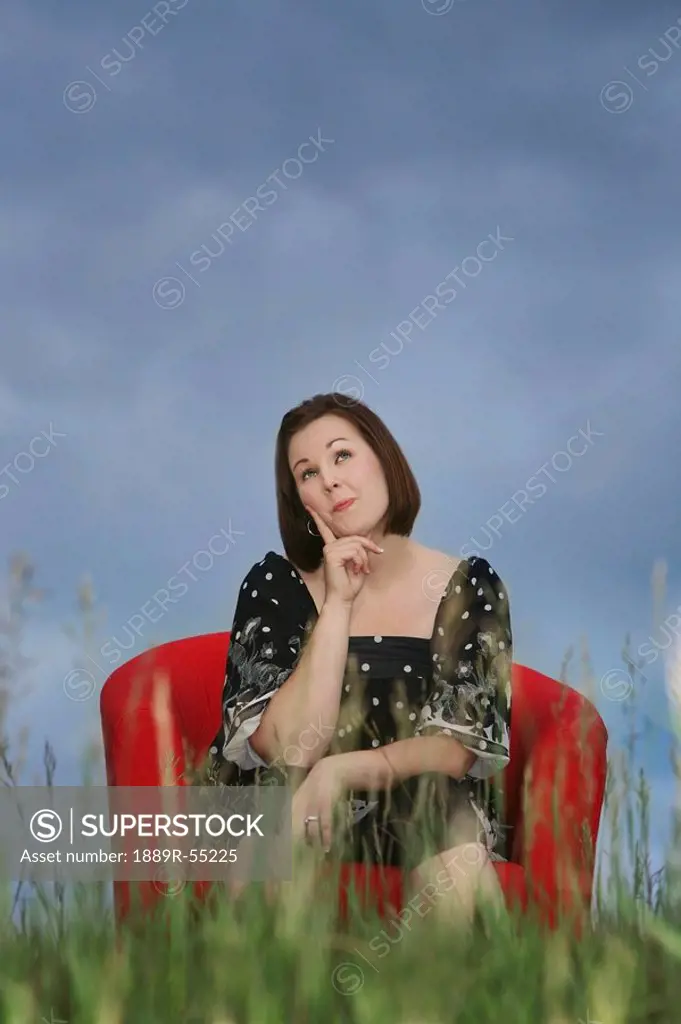 a woman sitting in a red chair in a field in a thinking pose
