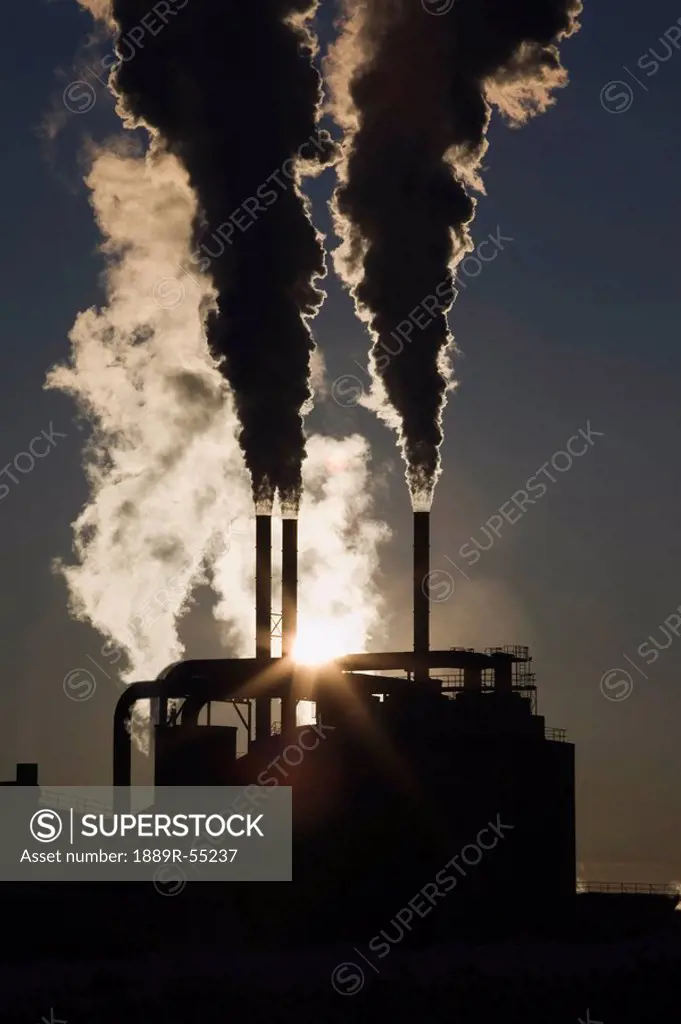 edson, alberta, canada, silhouette of smoke stacks with steam and a sunburst