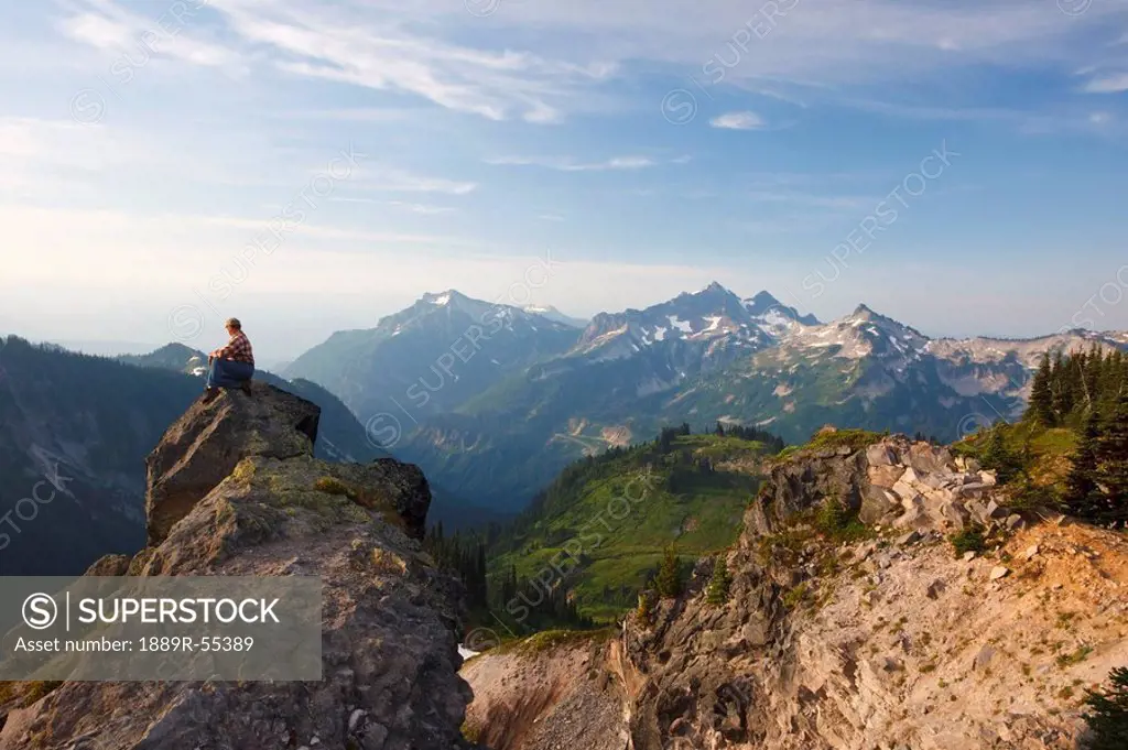 washington, united states of america, a man sitting on a rock overlooking the tatoosh mountains in paradise park in mt. rainier national park
