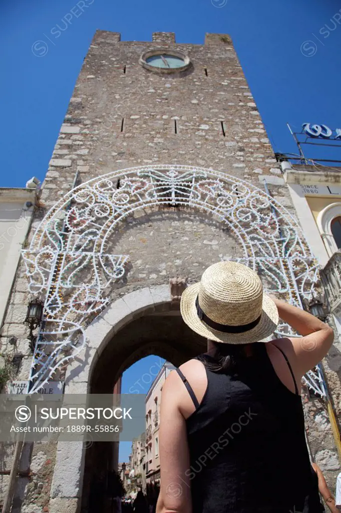female tourist looking at the clock tower of san giuseppe church, taormina, sicily, italy