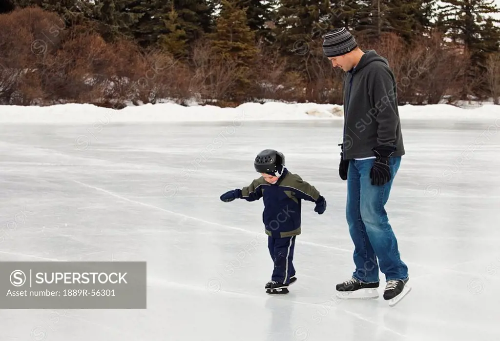 edmonton, alberta, canada, a father skates with his young son in hawrelak park on an outdoor ice rink