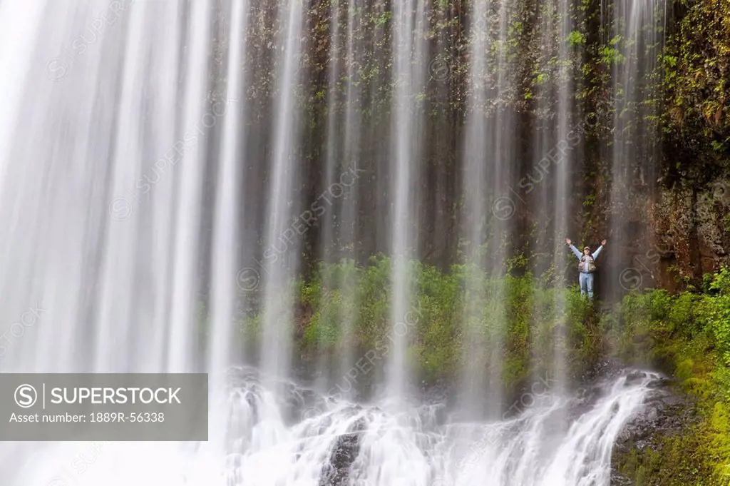 oregon, united states of america, a person with arms raised behind north middle falls in silver falls state park