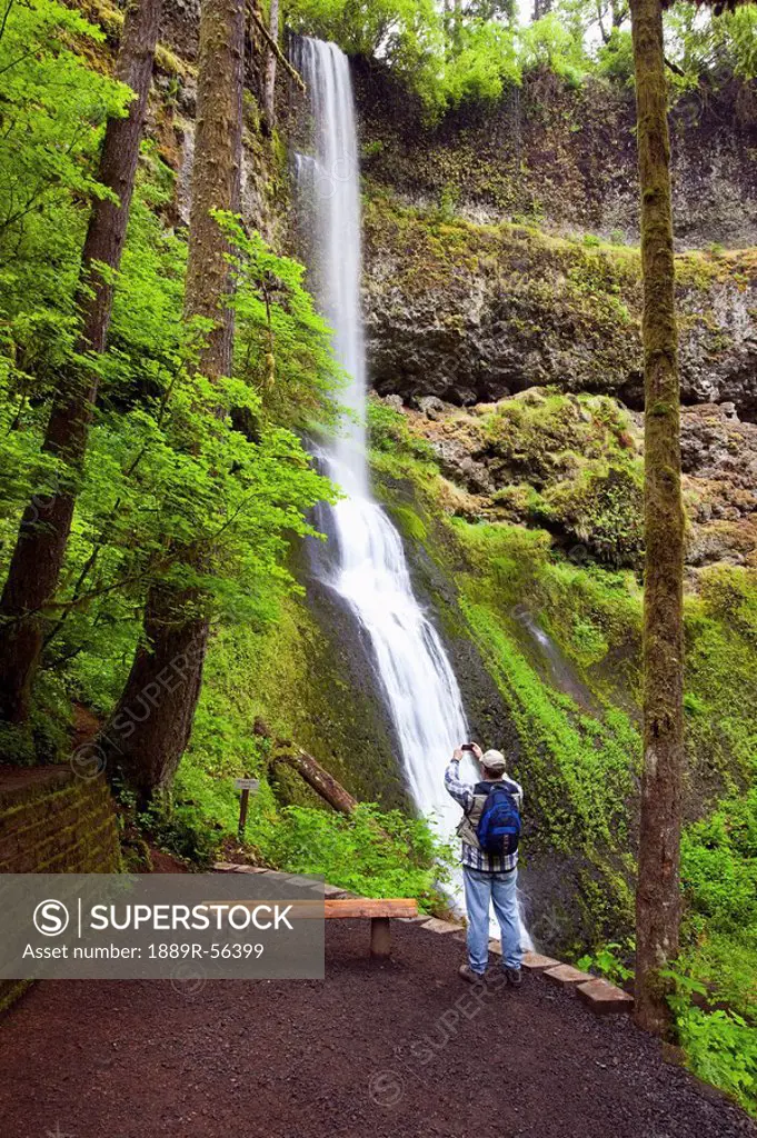 oregon, united states of america, a hiker taking a picture with his camera at winter falls in silver falls state park