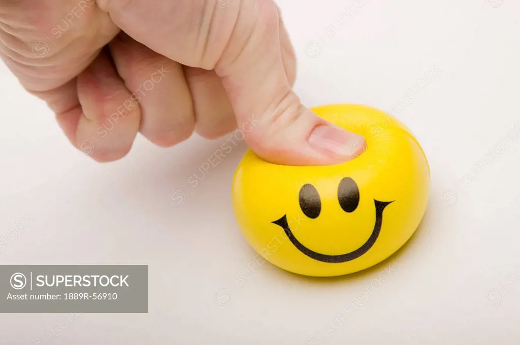 yellow happy face being squeezed by a thumb, edmonton, alberta, canada