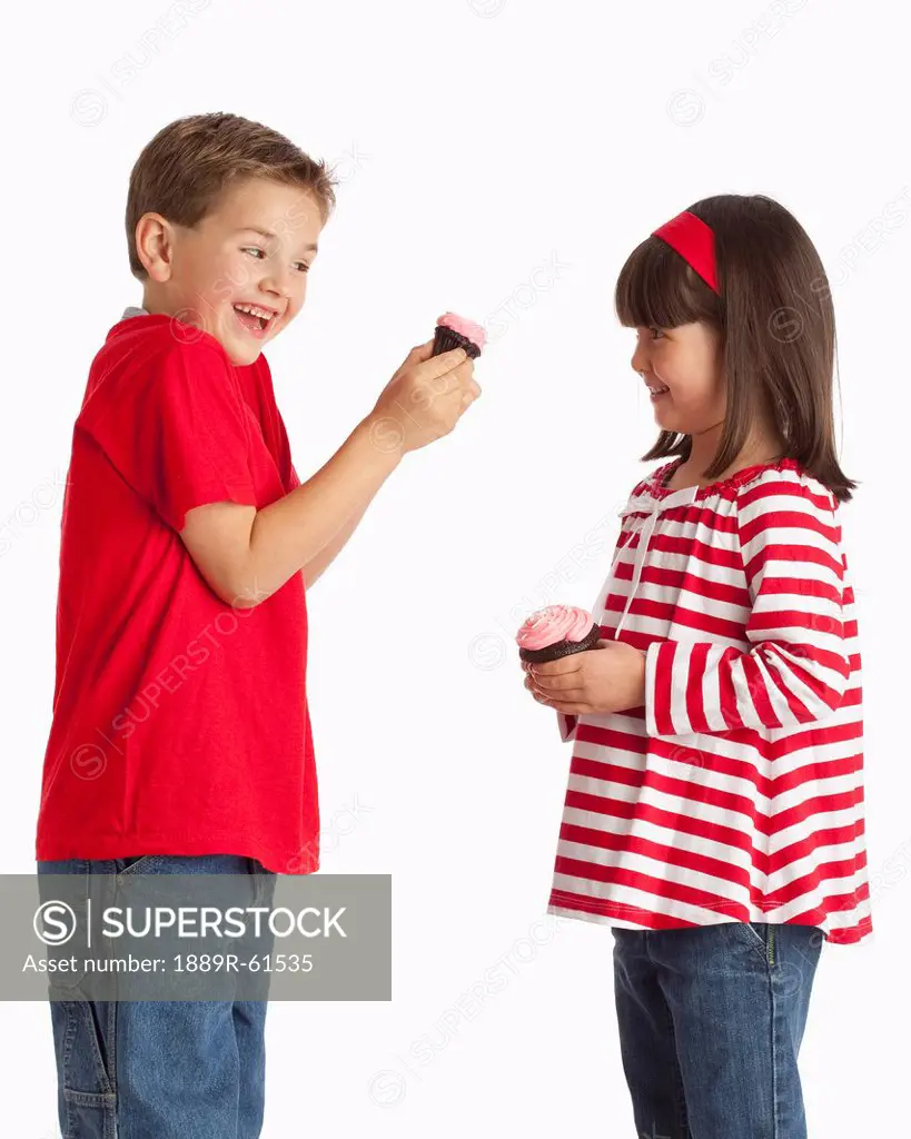 A Girl And Boy Holding Chocolate Cupcakes