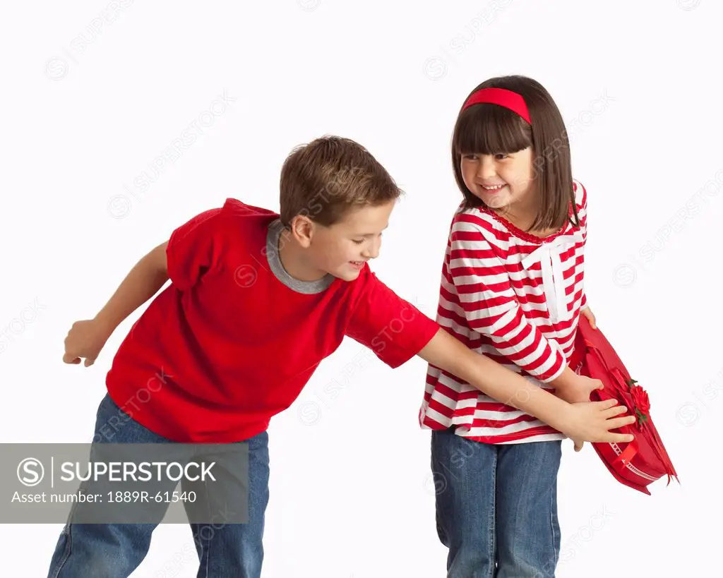 A Boy Reaching For A Heart Shaped Box That A Girl Is Holding Away From Him