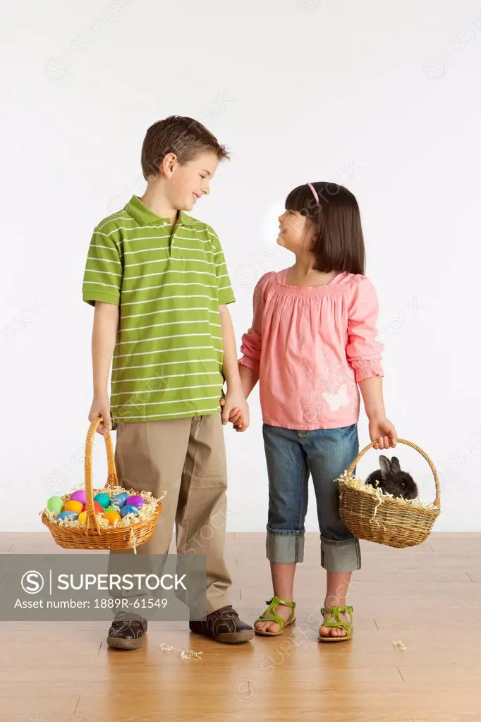 A Boy And Girl Holding Baskets With A Rabbit And Colorful Easter Eggs In Them